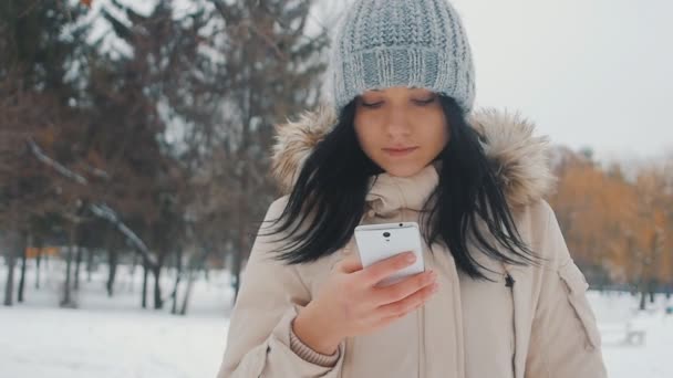 Retrato de mujer linda joven en el parque de invierno utiliza teléfono inteligente — Vídeos de Stock