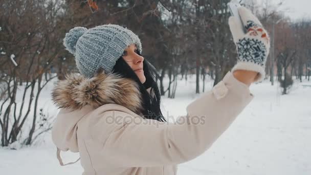 Young cute woman in winter park doing selfie with her smartphone — Stock Video