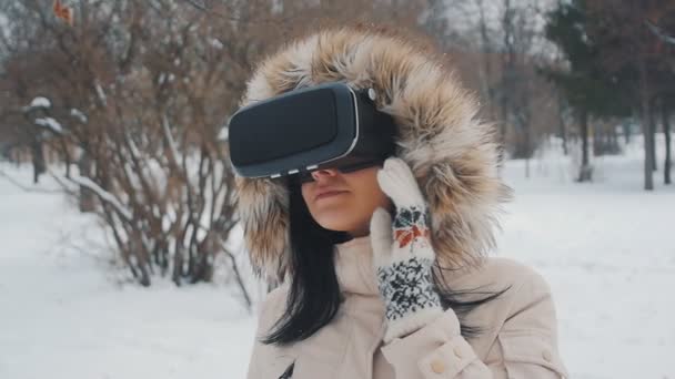 Фото девушки, получающей опыт использования VR-гарнитуры на открытом воздухе в зимнем парке — стоковое видео