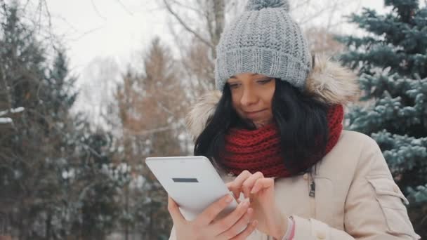 Молода мила дівчина в зимовому парку використовує планшетний ПК — стокове відео
