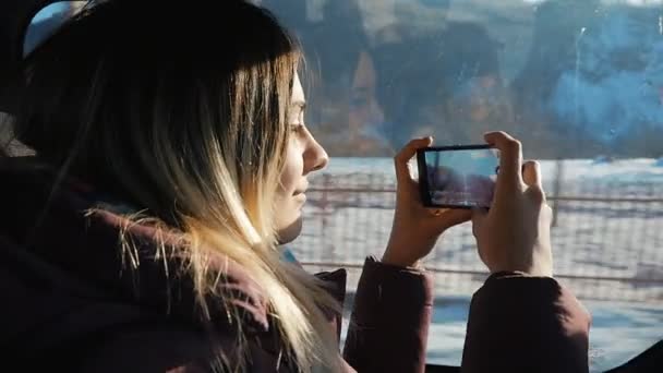 若い女性は、晴れた日に車で旅行します。彼女は窓の外見ているとスマート フォンを使用して写真をやって — ストック動画