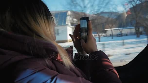 Junge Frau, die an einem sonnigen Tag mit dem Auto unterwegs ist. Sie schaut aus dem Fenster und macht Fotos mit dem Smartphone — Stockvideo