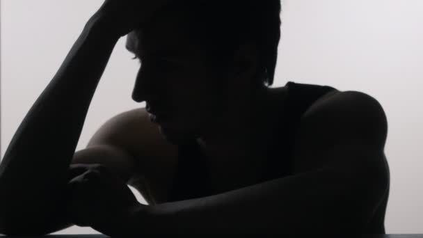 Silhouette eines depressiven, traurigen jungen Mannes, der am Tisch sitzt — Stockvideo