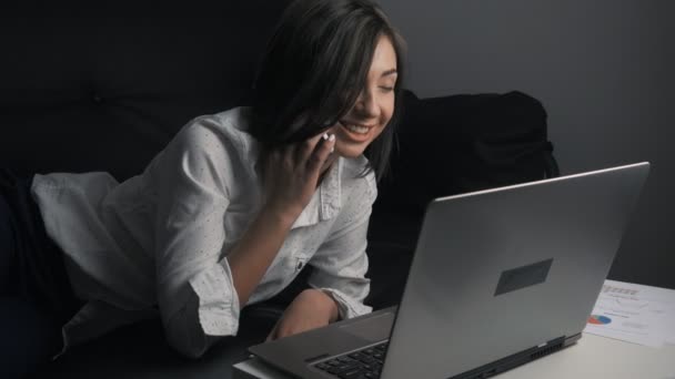Joven mujer de negocios tumbada en el sofá y trabajando en el ordenador portátil — Vídeo de stock