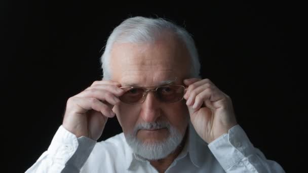 Close-up van portret van senior man zetten bril op zwarte achtergrond — Stockvideo