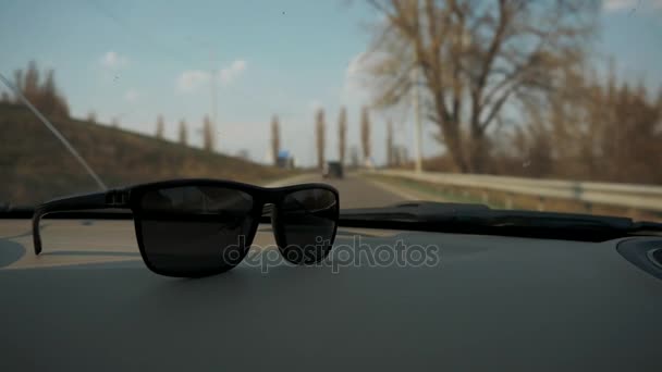 Samochód jeździ na autostradzie. Okulary przeciwsłoneczne leżą w pobliżu szkła. Wycieczka do odpoczynku — Wideo stockowe