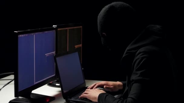 Hacker in balaclava kraken code met laptop en computers vanuit zijn kamer donker hacker — Stockvideo