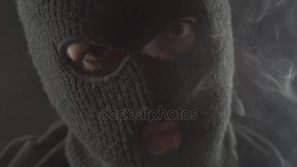 Farliga terroristen i en balaclava röker en cigarett och gör en massa rök. — Stockvideo