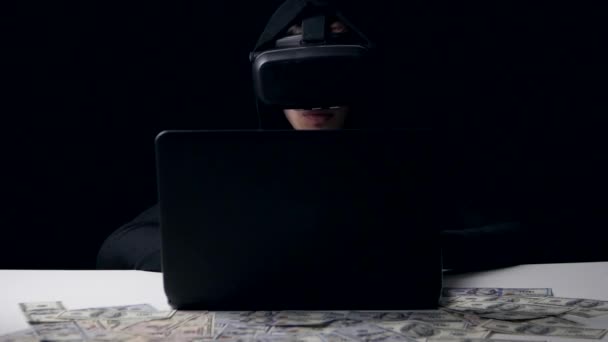 Hacker in de helm van virtual reality werken in donkere kamer. Hij telt geld. Computercriminaliteit. — Stockvideo