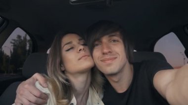 Genç çift aşk adam ve kız selfie arabada yapmak. Adam kızı sarılma