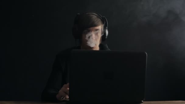 Bărbat în căști care lucrează la laptop și fumează țigară electronică — Videoclip de stoc