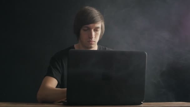 Чоловік працює на ноутбуці і курить електронну сигарету — стокове відео