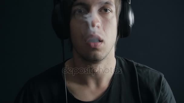 Jeune homme écoutant de la musique sur un casque et fumant une cigarette électronique — Video