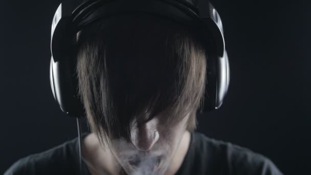 Νεαρό άνδρα να ακούτε μουσική με ακουστικά και το κάπνισμα ένα ηλεκτρονικό τσιγάρο — Αρχείο Βίντεο