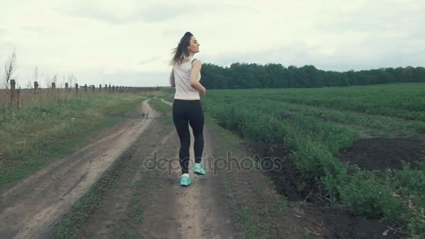 Gelukkig atletische meisje draait op weg in veld. buiten fitness. Geschoten met een steadicam — Stockvideo