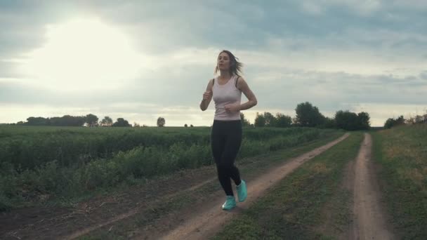 Hermosa chica haciendo jogging matutino al amanecer en el campo. Fitness al aire libre. Disparo con steadicam — Vídeos de Stock