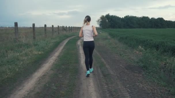 Atletische meisje draait op weg in veld. buiten fitness. Geschoten met een steadicam — Stockvideo