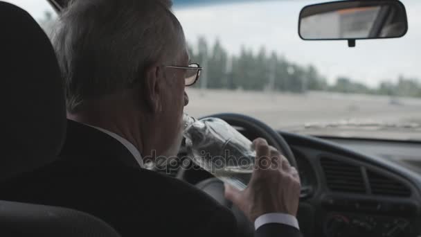 Hombre mayor bebe vodka mientras está sentado en el coche. Conductor borracho . — Vídeos de Stock