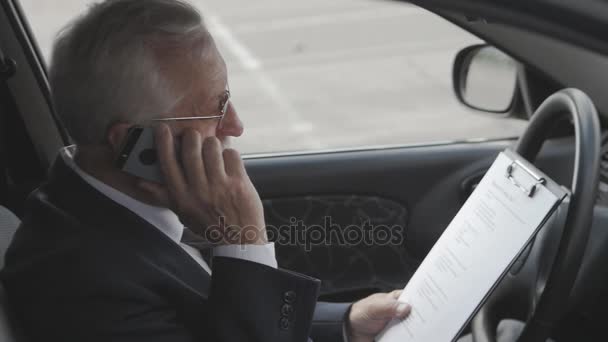 Człowiek starszy jest badanie dokumentów i rozmowy telefonicznej siedząc w samochodzie. Zajęty biznesmen. — Wideo stockowe