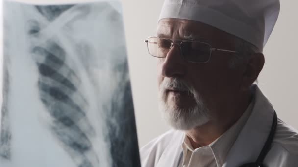 Vieux docteur avec des lunettes et une barbe regardant une radiographie — Video