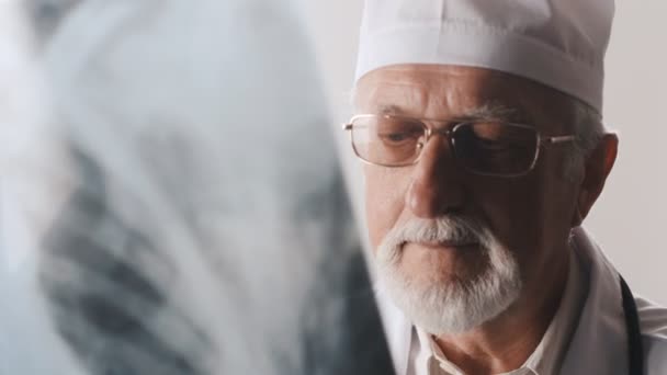 Старый доктор в очках и с бородой смотрит рентген — стоковое видео