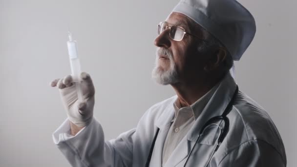 Ritratto di un medico anziano con barba e occhiali. Il medico tiene una siringa tra le mani. Trattamento con iniezioni . — Video Stock