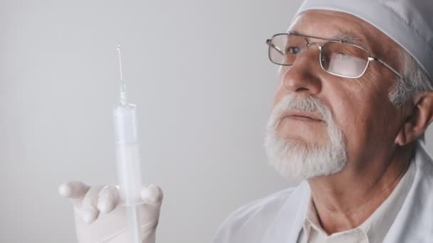 Close up of an elderly doctor with a beard and glasses. Medical worker holds a syringe in his hands. Treatment with injections. — Stock Video
