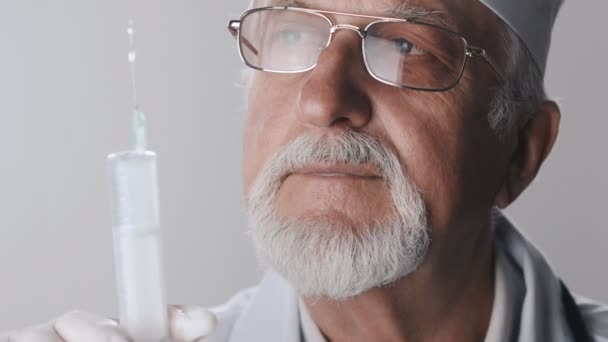 Yaşlı doktorun sakal ve gözlük ile kapatın. Tıbbi çalışan bir şırınga elinde tutar. İğneleri ile tedavi. — Stok video