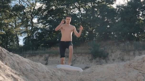 Mann springt frontal auf den Strand bei Sonnenuntergang. Freerunner springt akrobatischen Stunt — Stockvideo