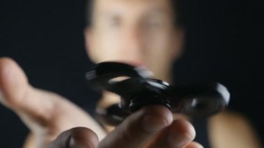 Topluca spinner ile oynayan adam. El altında siyah arka plan üzerinde dönen değer değişimi veya Kıpırdanmayı el oyuncak yakından mans