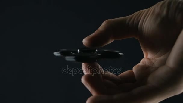 Närbild spinner eller fidgeting hand leksak roterar på mans hand på svart bakgrund — Stockvideo