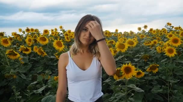 Portrait of a young woman in a white tank top in a field of sunflowers. Storm clouds on the background. — Stock Video