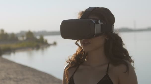 Fiatal nő a bikini használ egy virtuális valóság szemüveg a strandon. Szexi lány kezd tapasztalattal rendelkezik a Vr-headset nyári tengeri háttér. — Stock videók
