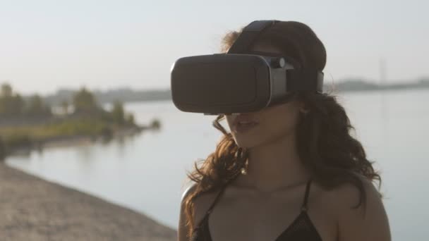 Mladá žena v bikinách na pláži používá virtuální realita brýle. Sexy dívka se zkušenostmi v používání Vr headset na léto na pozadí moře. — Stock video