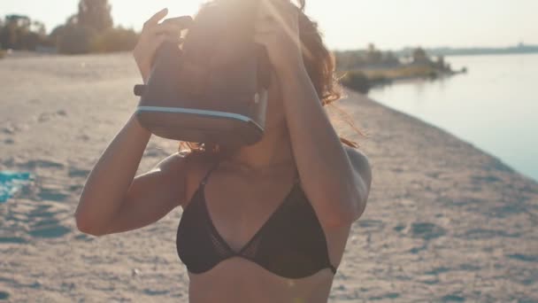 Mladá žena v bikinách na pláži používá virtuální realita brýle. Sexy dívka se zkušenostmi v používání Vr headset na léto na pozadí moře. — Stock video