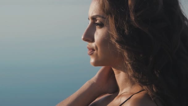Schattige brunette meisje in een zwarte bikini op het strand op de achtergrond van de zee. — Stockvideo