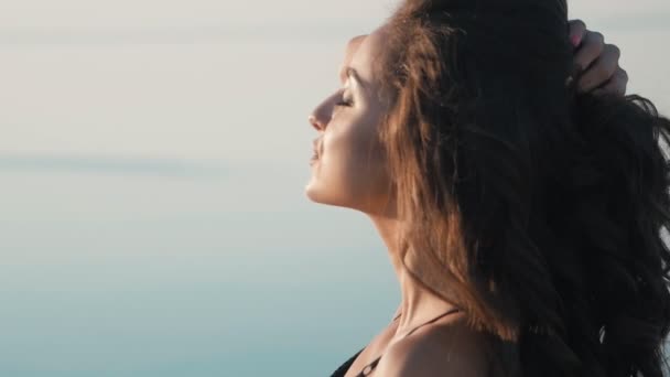 Close-up van portret van brunette meisje in een zwarte bikini op het strand op de achtergrond van de zee. — Stockvideo