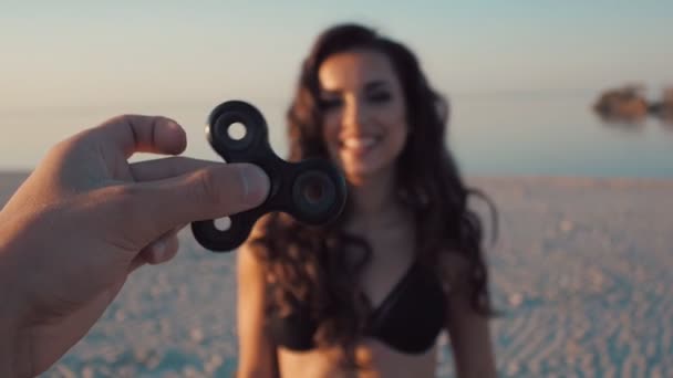 Spinner or fidgeting hand toy rotating on manss hand. Young sexy happy woman smiling on background. Girl spinning spinner — Stock Video