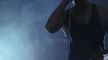 Erkek şarkıcı mikrofona doğru söylüyor. Şarkıcı sanatçı sahnede konser rock bant. Müzik video punk, ağır metal veya rock grubu