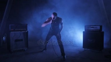 Erkek vokalist mikrofona doğru söylüyor. Şarkıcı sanatçı sahnede konser rock bant. Müzik video punk, ağır metal veya rock grubu