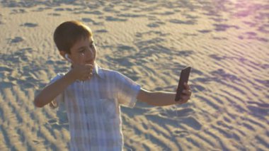 Çocuk selfie sahilde kum bir arka plan üzerinde bir smartphone kullanarak yapıyor