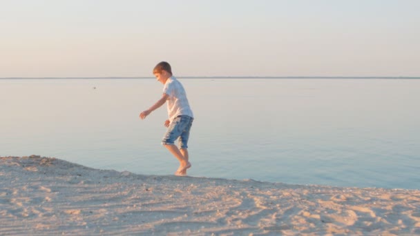 Niño en una camisa blanca en una playa de verano al atardecer — Vídeos de Stock