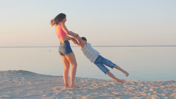 Vacaciones familiares. feliz mamá e hijo tonto alrededor en la playa contra el telón de fondo del mar . — Vídeos de Stock