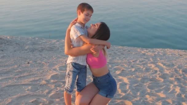 Любящая мать обнимает своего сына на морском фоне — стоковое видео