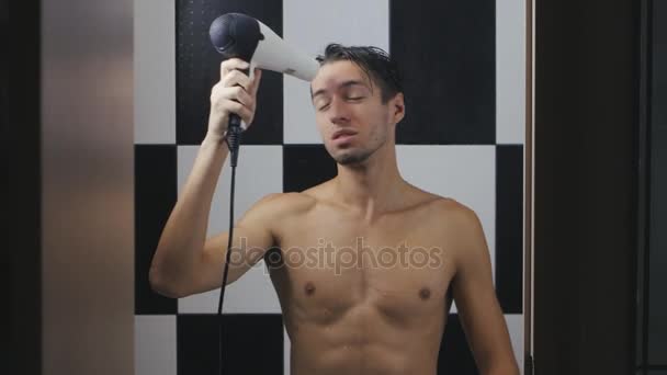 Молодой человек сушит волосы в ванной — стоковое видео