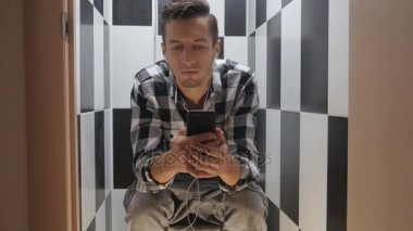adam tuvalette oturmuş müzik dinlerken kulaklık