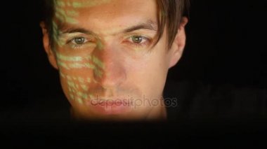 Oda karanlık ofis onun yüzünde yeşil kod karakterlerini yansıtan iken bir bilgisayarda çalışan adam programcı hacker.