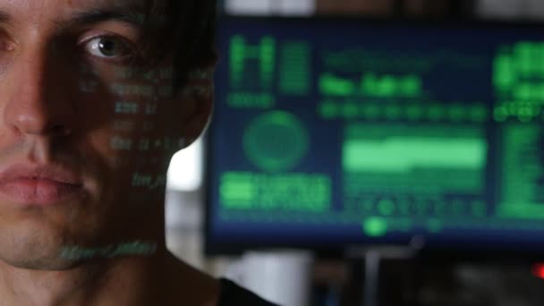 Retrato del hombre programador hacker con caracteres de código verde reflejan en su cara con una computadora en el fondo — Vídeo de stock