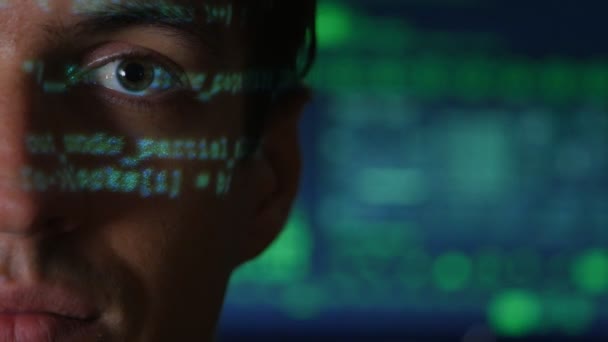 Портрет человека программиста хакер с зеленым кодом символов отражается на его лице с экраном компьютера на заднем плане — стоковое видео