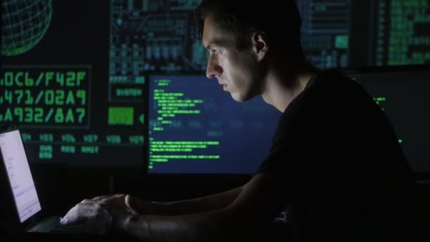 Портрет молодого программиста, работающего за компьютером в дата-центре, заполненном экранами — стоковое видео